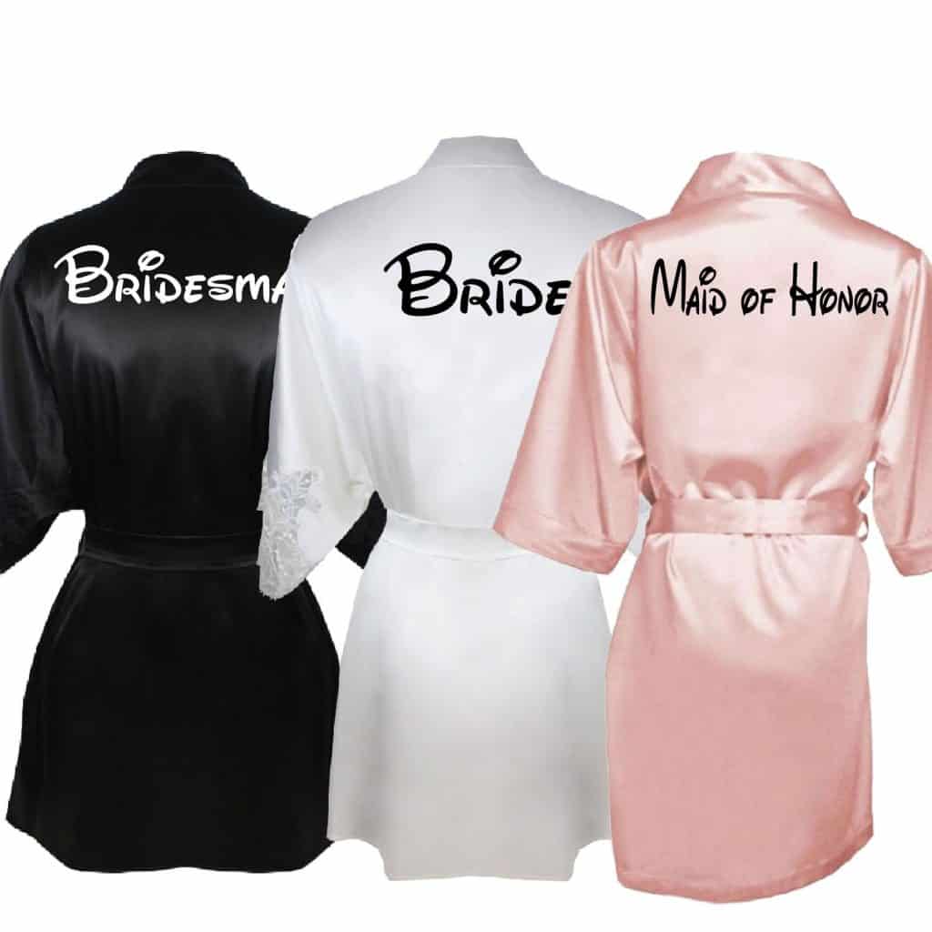 Trio of satin robes against a white background. First robe is black, second is white, third is pink.