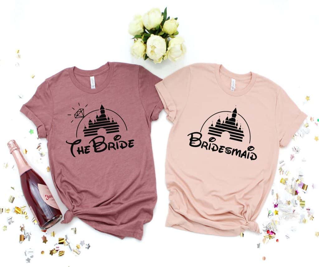 Flat lay of two shirts. One is maroon and has "The Bride" in Disney font in black. The other shirt is pink and has "Bridesmaid" in Disney font in black.