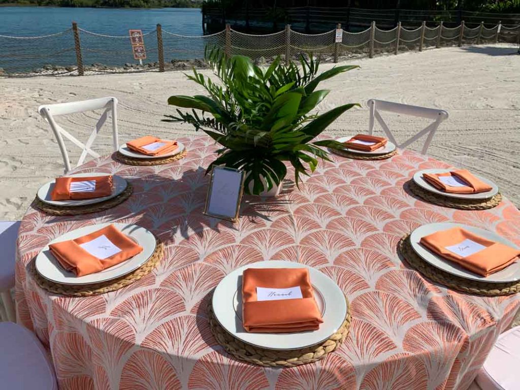 Wedding reception table with orange lace tablecloth and orange folded napkins