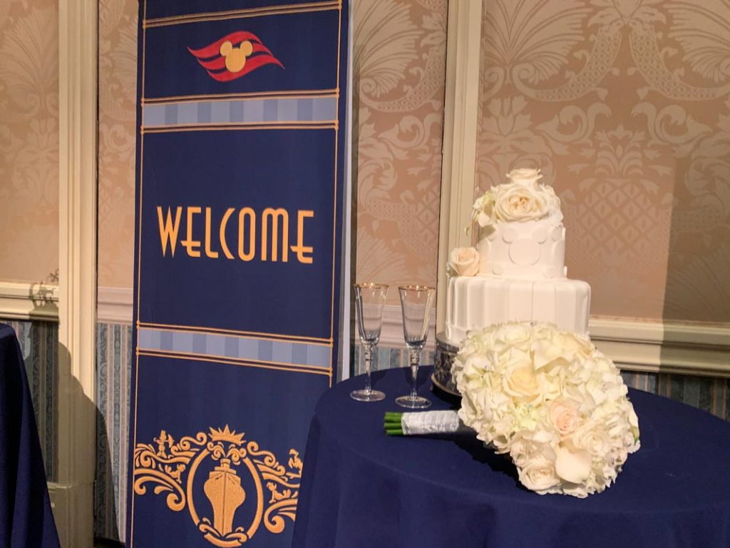 Disney Cruise Line sign that reads "welcome" next to white two tier wedding cake