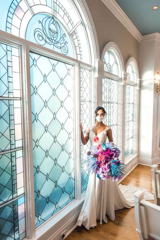 Woman wearing wedding gown and white face mask and holding colorful bouquet