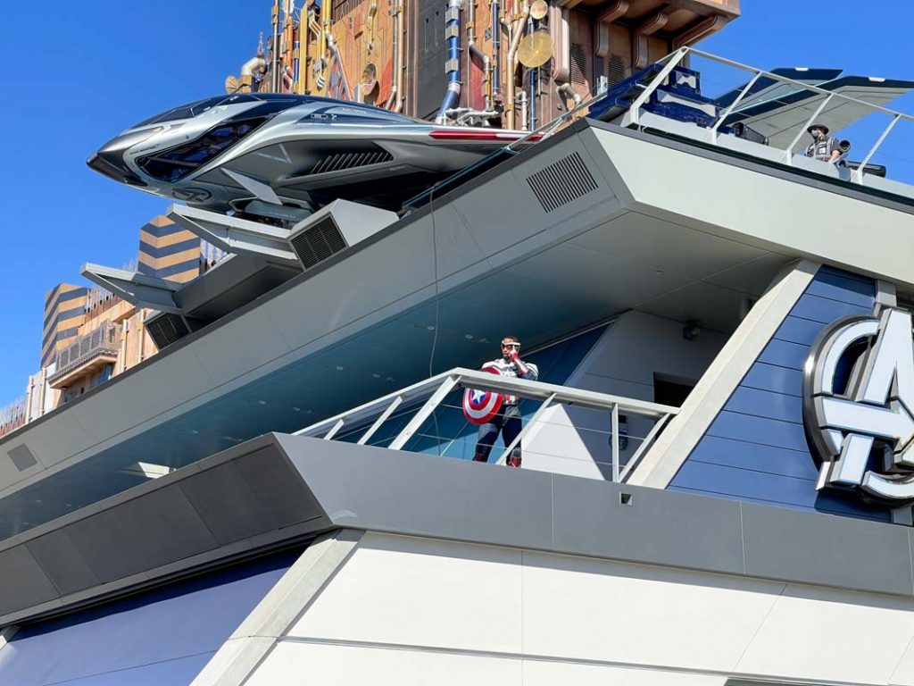 Captain America standing at the top of the Avengers Headquarters building at Avengers Campus