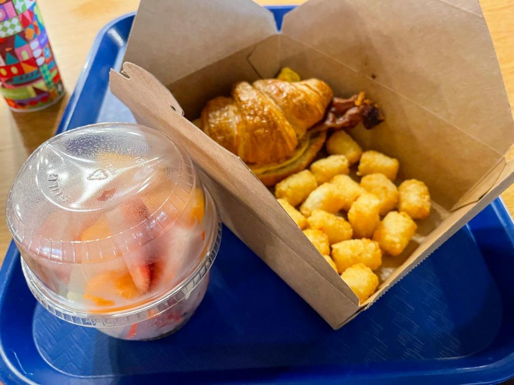 Blue tray with breakfast sandwich, tater tots, and cup of fruit