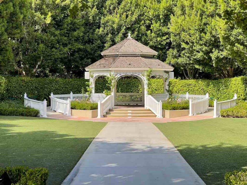 Rose Court Garden featuring white gazebo with brown roof surrounded by green shrubs and rose bushes