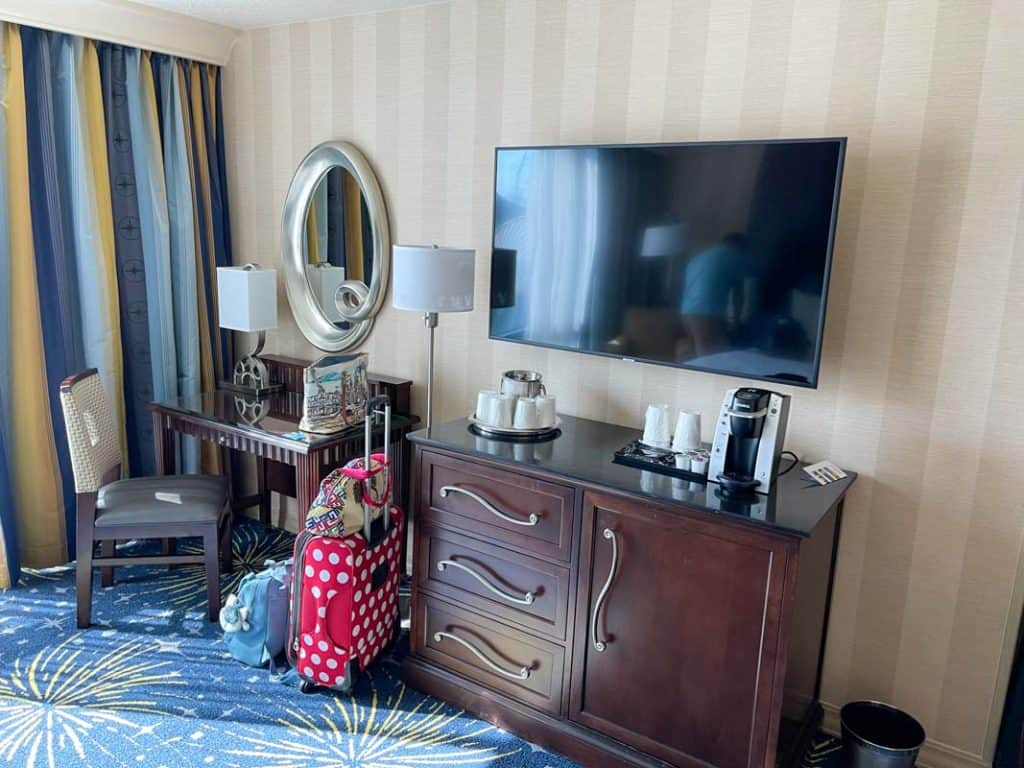 Interior of Disneyland Hotel room showing dresser drawers, coffee maker, desk, and wall mounted TV