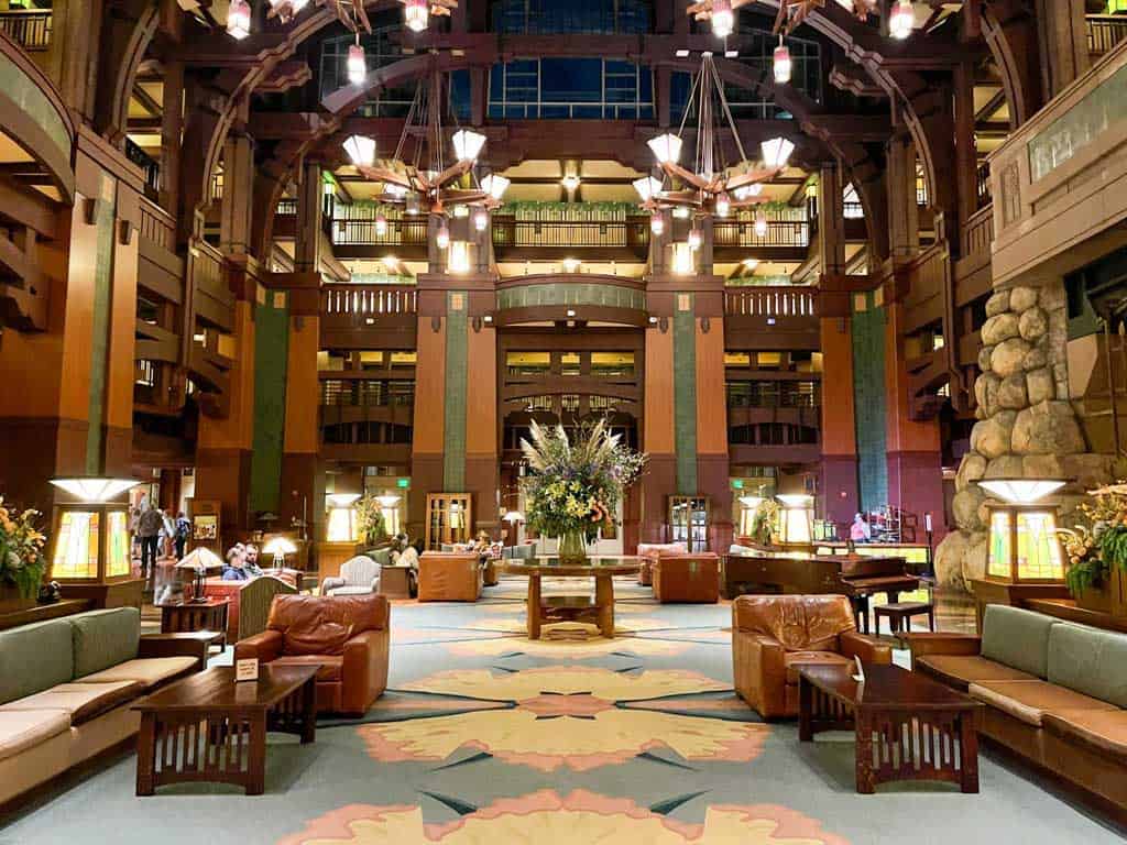 Large hotel lobby with high ceilings and brown furniture sitting atop carpet with muted colors.