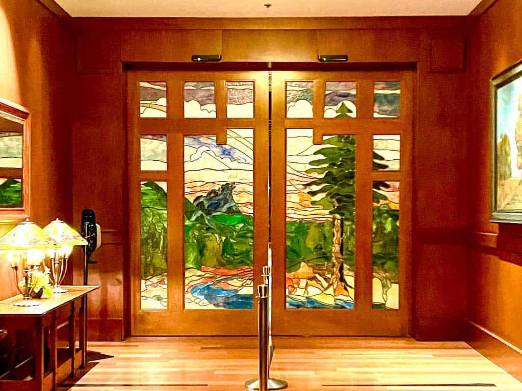 Automatic sliding doors featuring stained glass depicting Grizzly Peak from Disney California Adventure. The doors have brown wood trim.