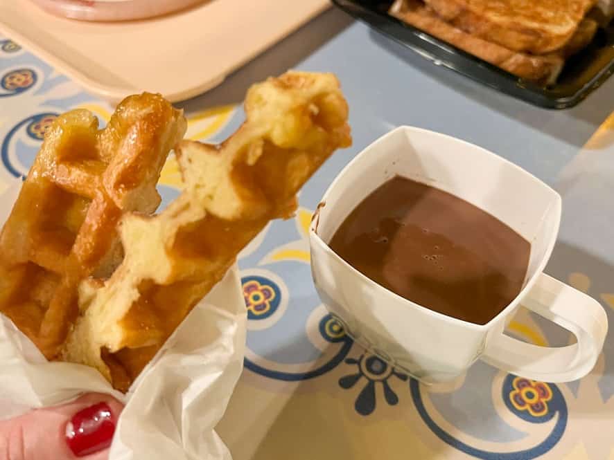Two waffle sticks next to a cup of sipping chocolate