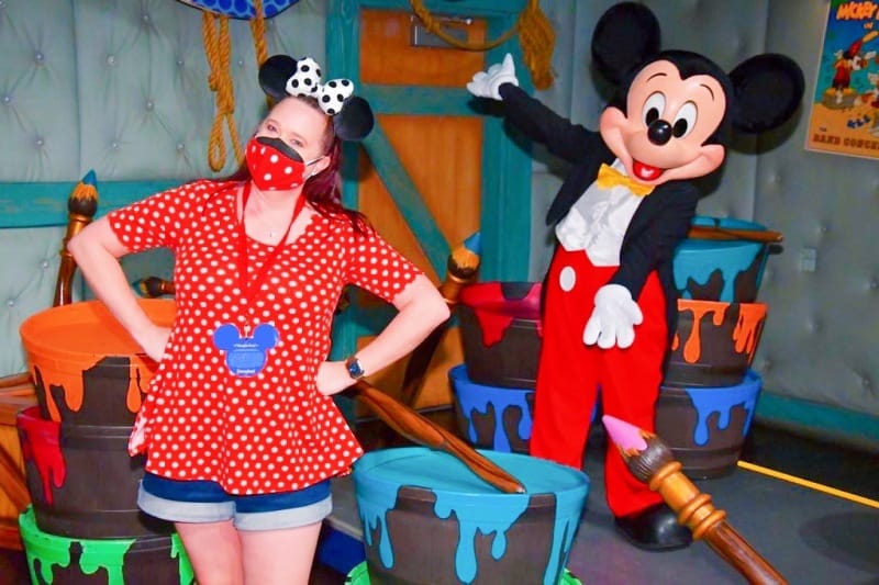 Woman wearing red and white polka dot shirt poses with Mickey Mouse at Disneyland