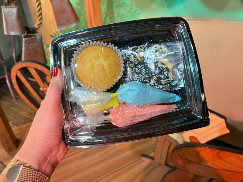 Close up of cupcake decorating kit with vanilla cupcake, frosting bags, and sprinkles