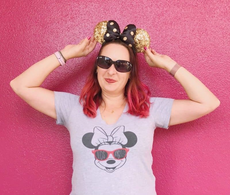 woman wears gold and black Minnie Mouse ear headband against pink wall