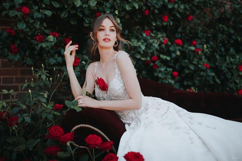 woman wears white bridal gown while surrounded by red roses