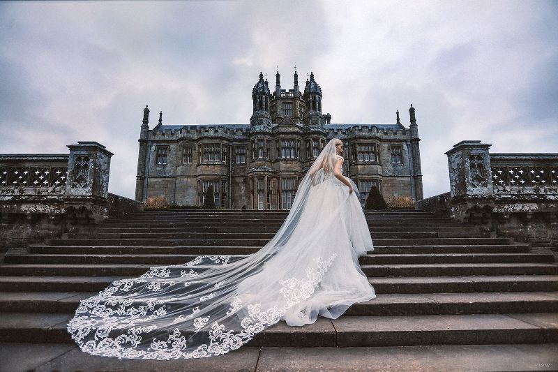 woman wearing wedding dress on the steps in front of a castle
