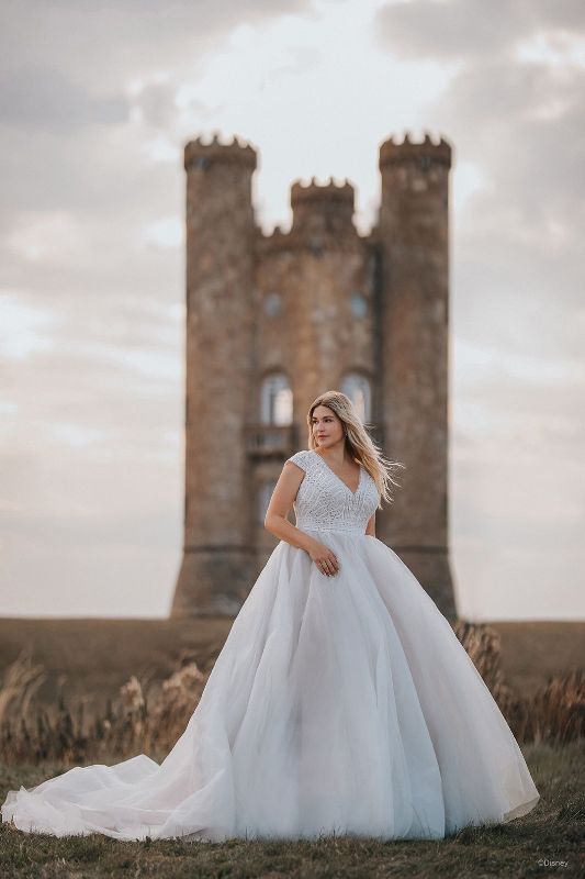 Plus size woman wears white sleeveless wedding gown with castle in the background