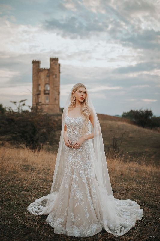 Bride wears fit and flare wedding gown with long veil with castle in the background