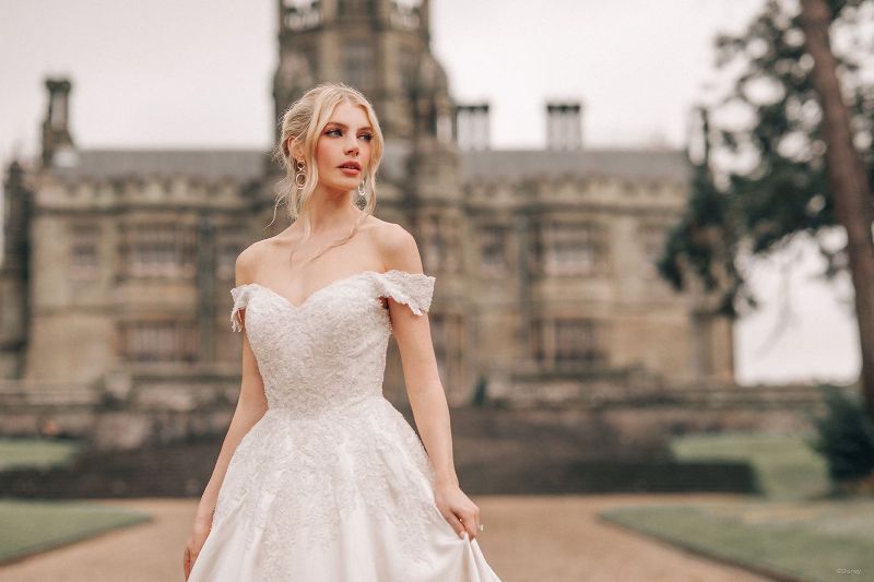 Woman wears off shoulder wedding gown in front of castle