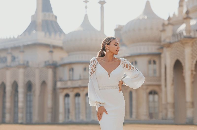 Bride wears wedding dress with cuffed sleeves in front of palace