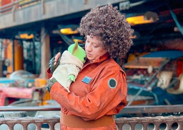 Woman in Peli Motto costume holding Grogu plush like a baby