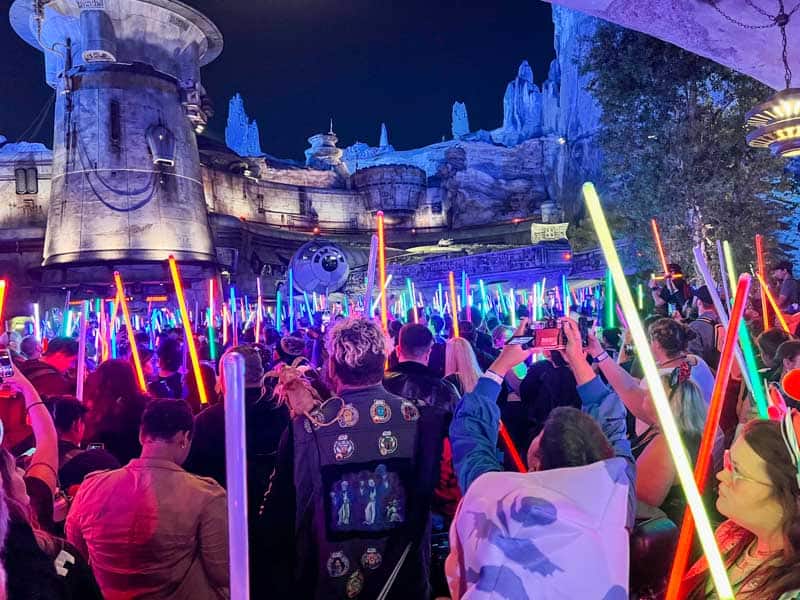 Hundreds of people holding lightsabers gather in front of the Millennium Falcon at Disneyland
