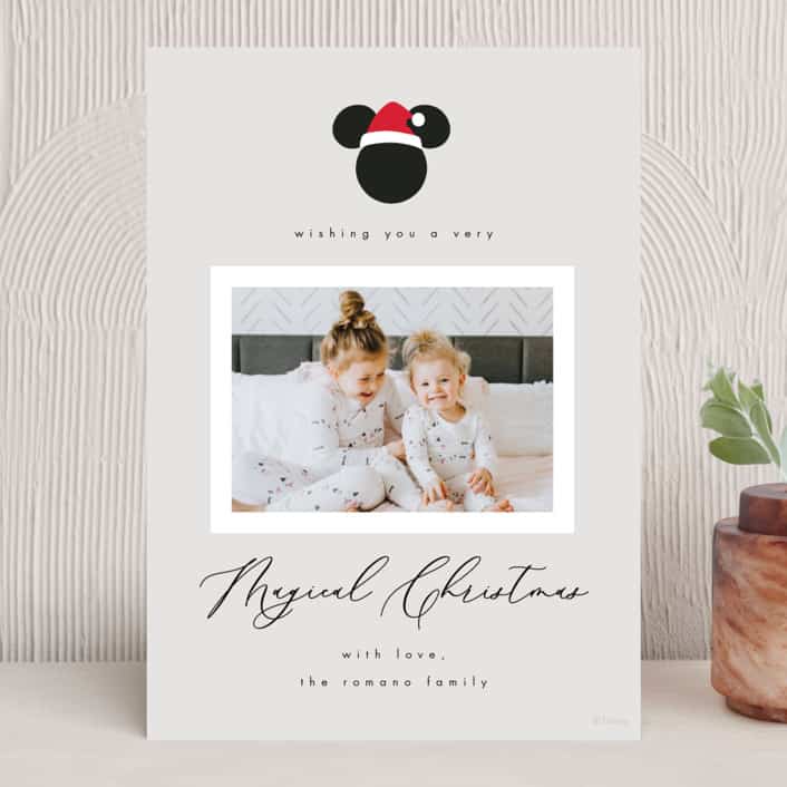 Off white holiday card with Mickey head shape on top wearing santa hat and family photo below