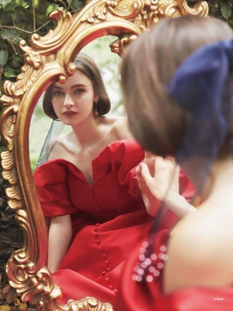 Woman wears red ballgown inspired by Snow White; she is looking in the mirror and the photo is of her reflection