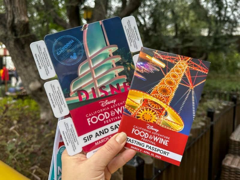 A hand holds up the Sip and Savor Pass and Tasting Passport from Disney California Adventure Food and Wine Festival