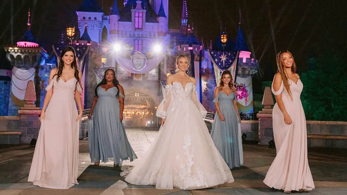 Models wear Disney wedding gown and bridesmaid gowns in front of Sleeping Beauty Castle