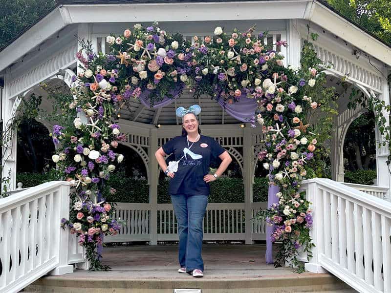 Woman wearing black shirt and jeans stands on the steps of the Rose Court Garden gazebo