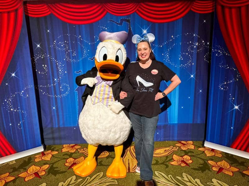 Woman in black shirt poses with Donald wearing a tuxedo in front of blue background