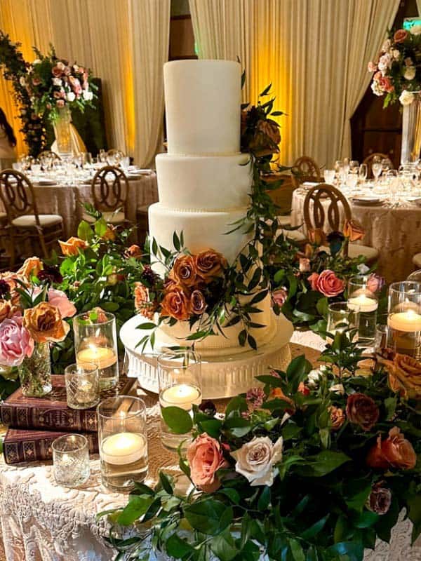 White four tier wedding cake decorated with toffee colored roses and greenery