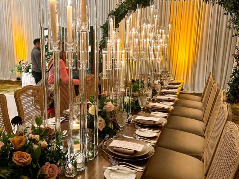 Close up of wedding reception table showing several high glass candle holders as centerpieces