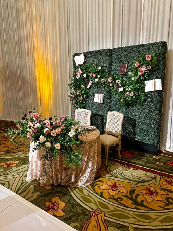 Sweeheart table at wedding reception with faux greenery hedge behind it