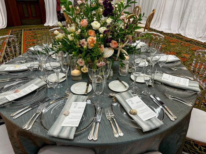 Wedding reception table with light blue table cloth and beach and white floral centerpiece