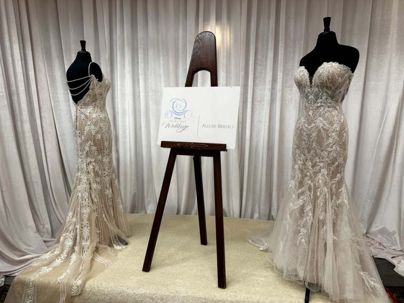 Two mannequins wearing white wedding gowns with a sign on an easel placed between them