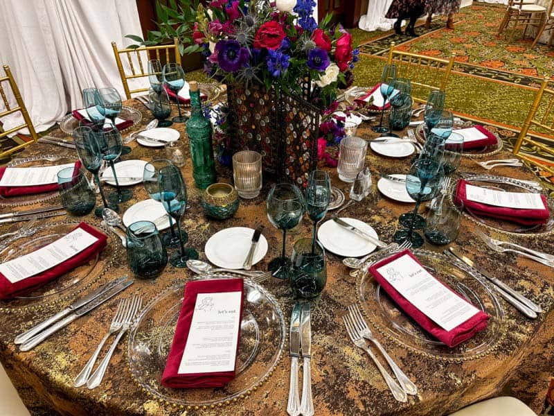 Wedding reception table with bronze tablecloth and purple and red floral centerpiece