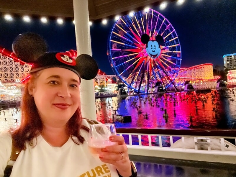 a woman holding a glass of wine in front of a ferris wheel at Disney California Adventure