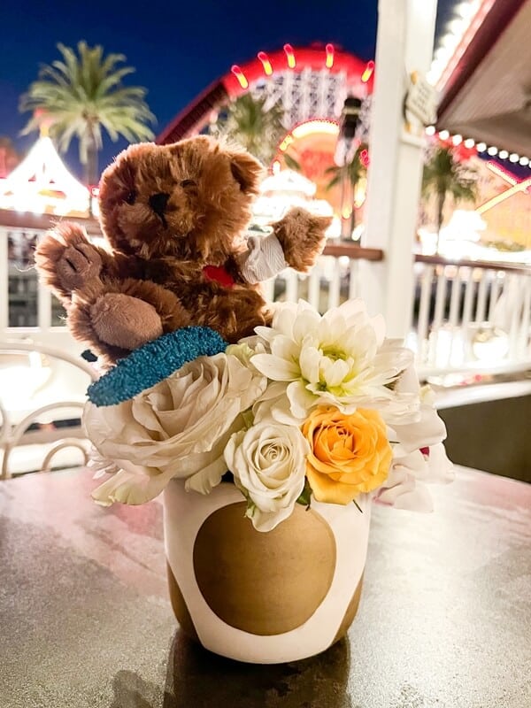 a teddy bear sitting on top of a vase filled with flowers.