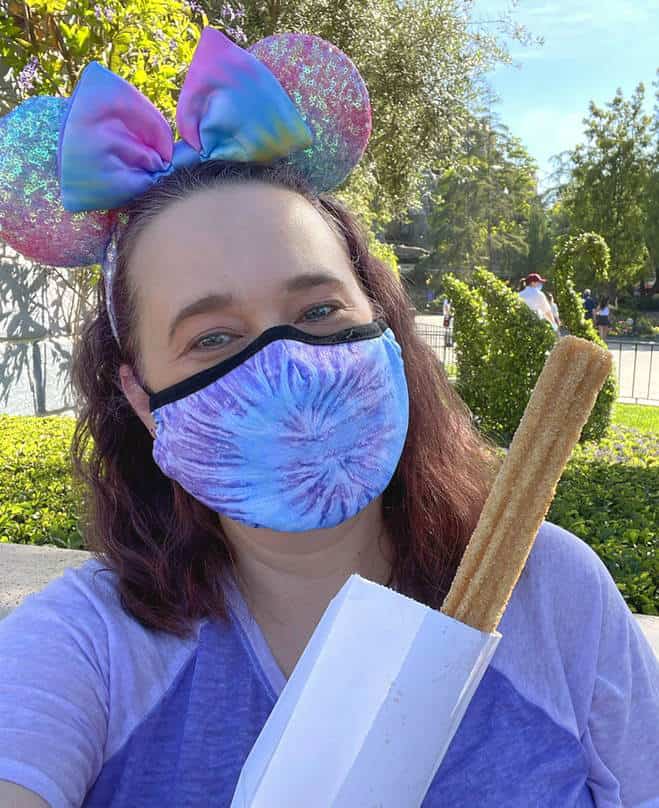 a woman with a face mask holding a churro at Disneyland