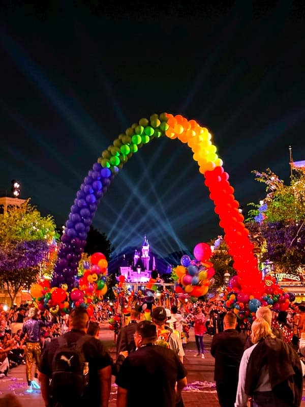 a group of people standing under a rainbow balloon arch at Disneyland