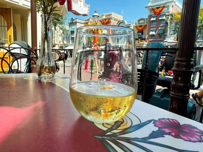 A glass of wine on a table in front of Carnation Cafe at Disneyland Park.