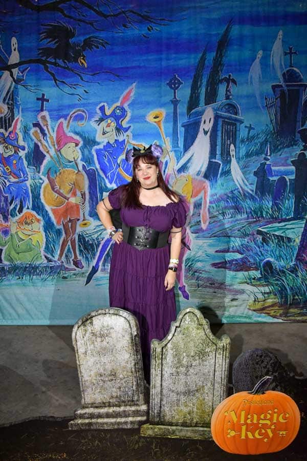 A woman in a purple dress standing in front of a graveyard backdrop at the Oogie Boogie Bash.