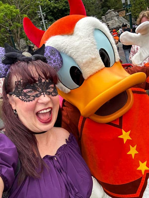 A woman is posing with Donald Duck at the Oogie Boogie Bash.