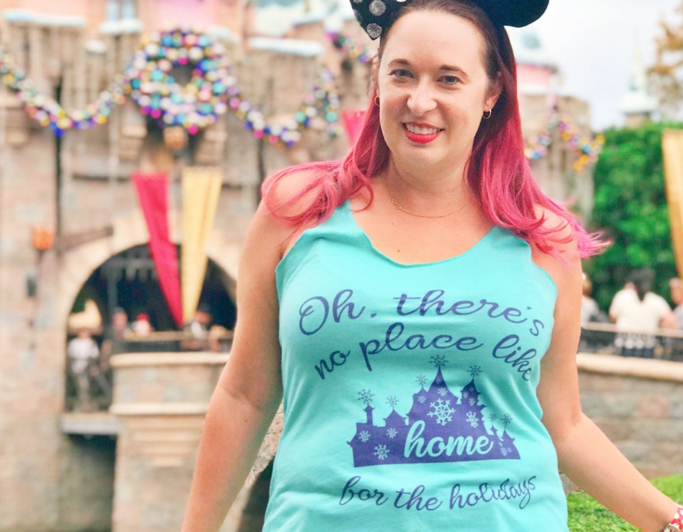 Woman wears light blue tank top that reads "Oh There's no place like home for the holidays" with a picture of a castle
