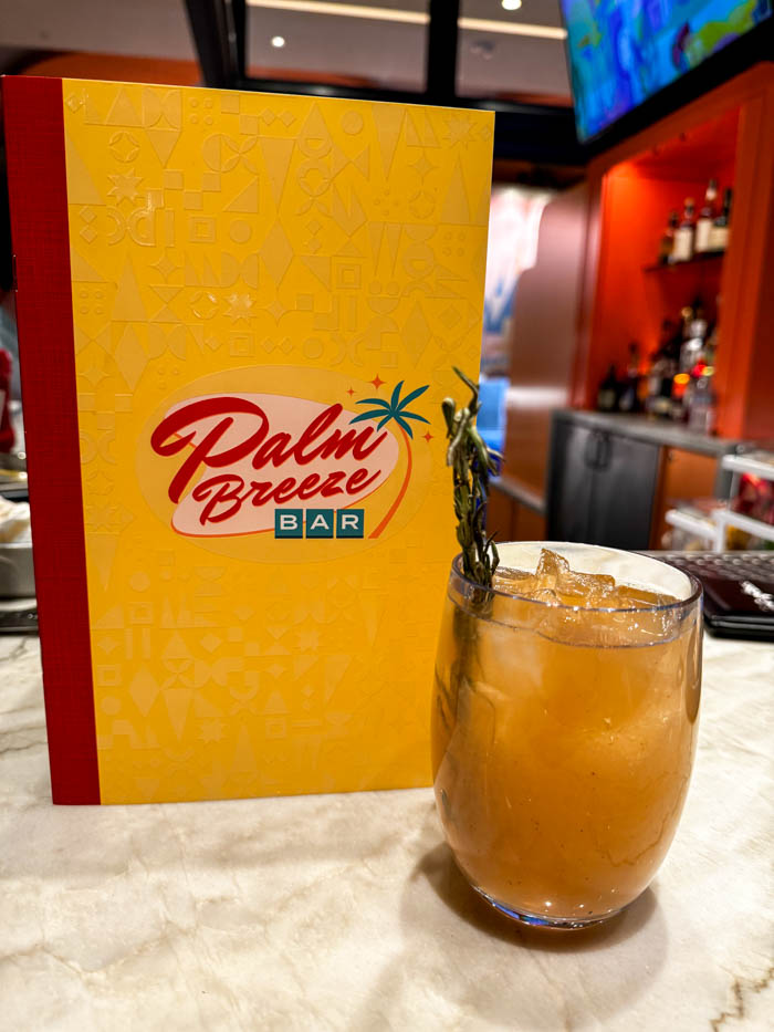 An orange cocktail sits in front of the Palm Breeze Bar menu