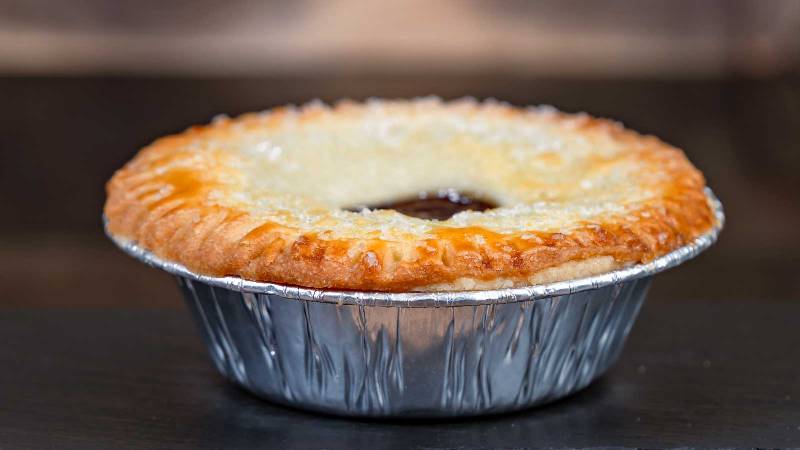 A pie in a foil cup sitting on a wooden table
