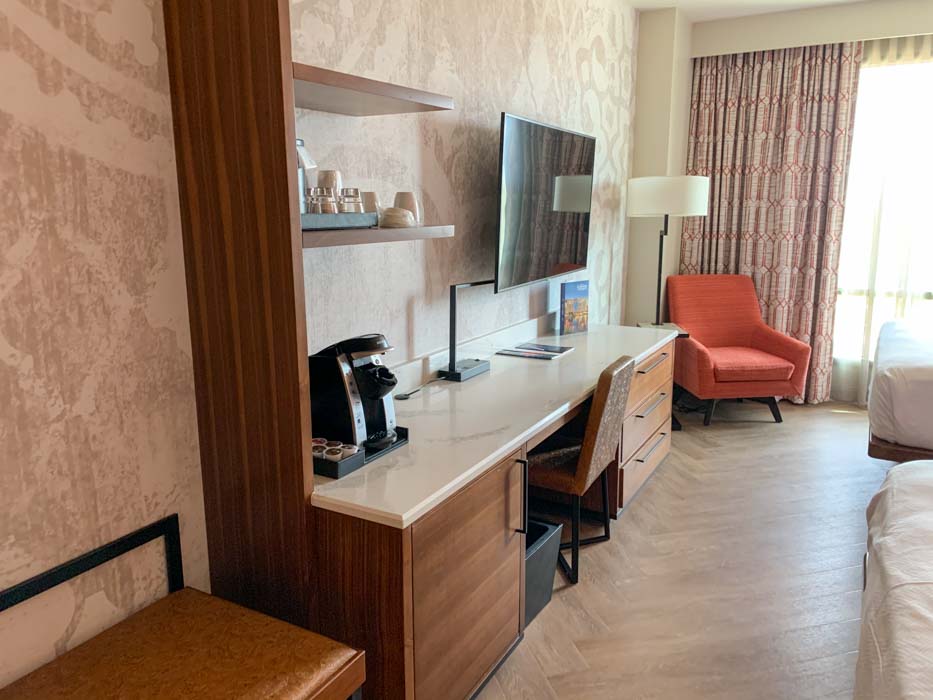 Interior of standard room at Gran Destino Tower showing a desk, flat panel TV, and orange armchair