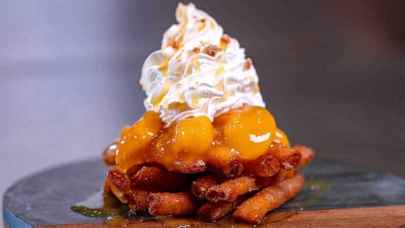 A stack of funnel cake fries topped with peaches and whipped cream